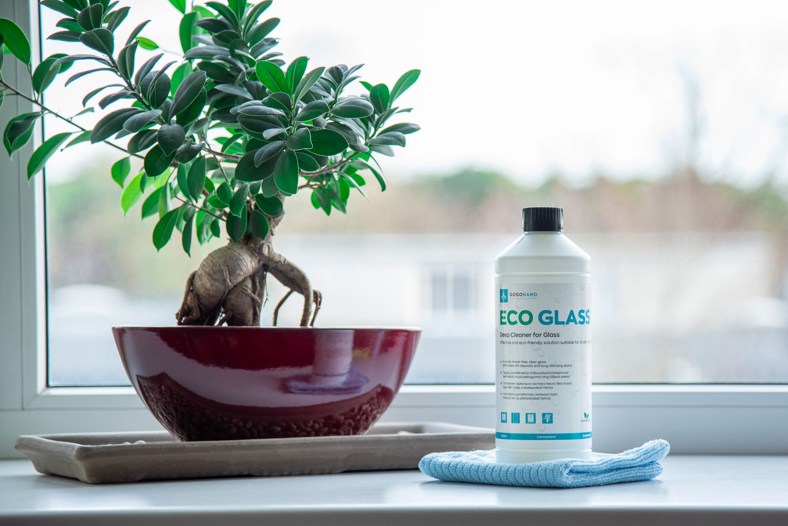 Eco-friendly glass cleaner and microfibre cloth beside a plant on a windowsill