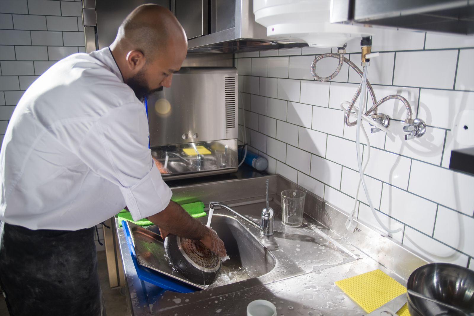 Chef cleaning cookware at a stainless steel sink in a commercial kitchen