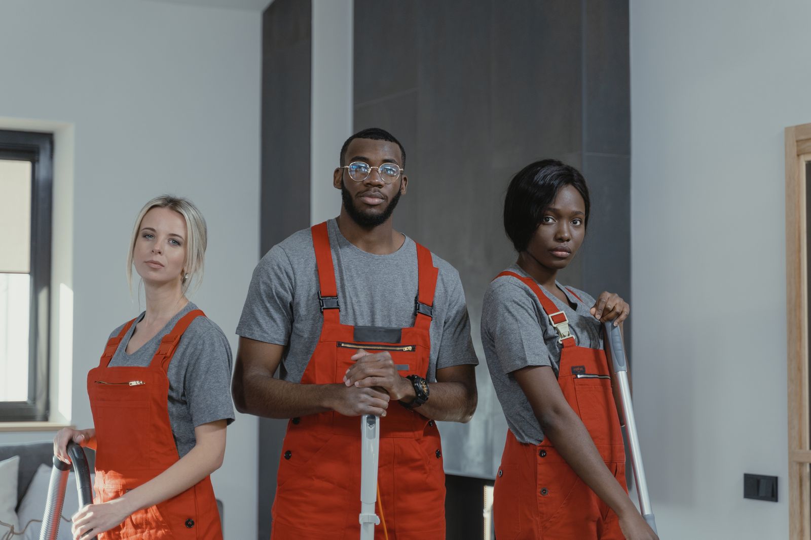 Three uniformed cleaners with mops and vacuum in a modern home