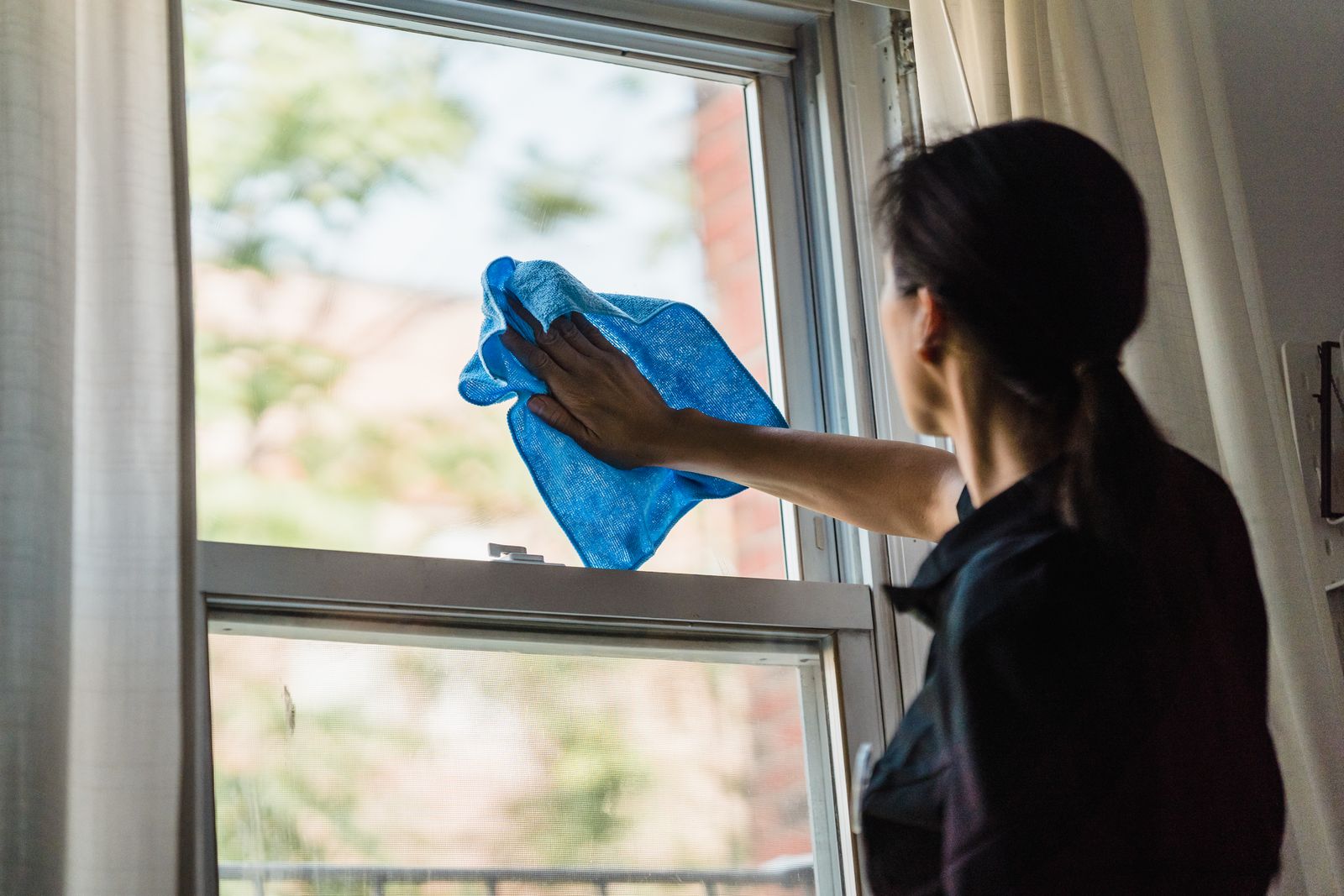 Cleaner wiping an interior window with a blue microfibre cloth